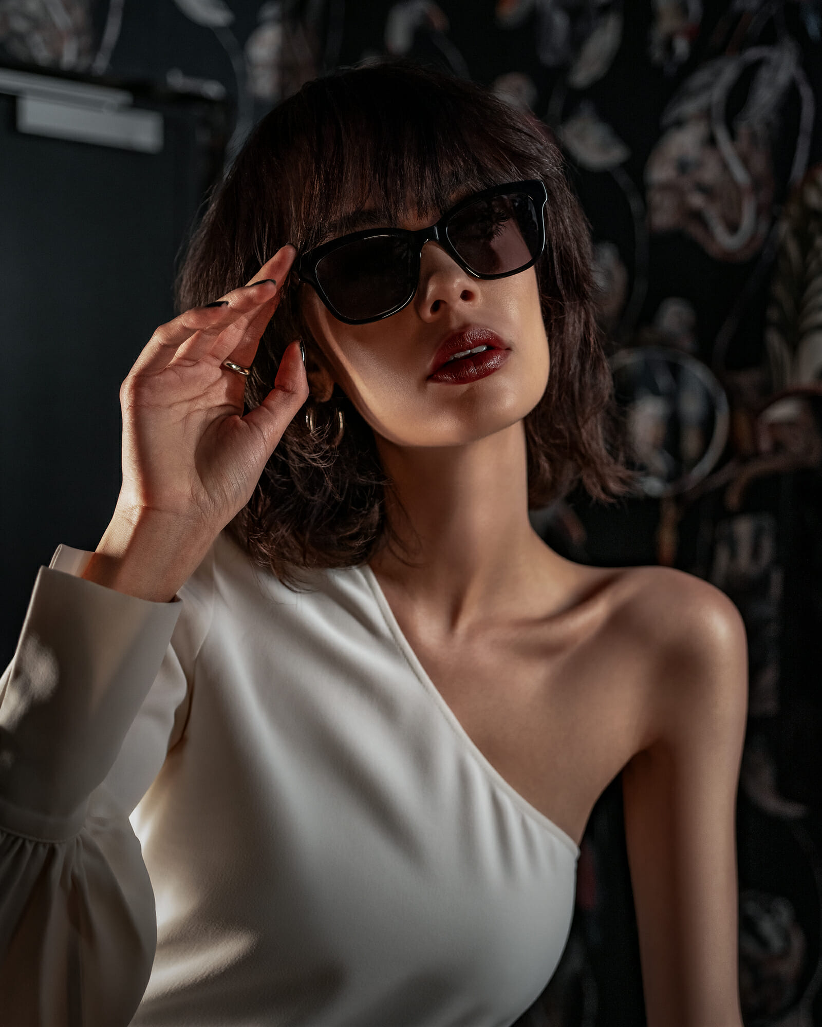 Portrait of a brown haired woman. She is wearing a black acetat shade, dark red lipstick and an elegant white blouse.
