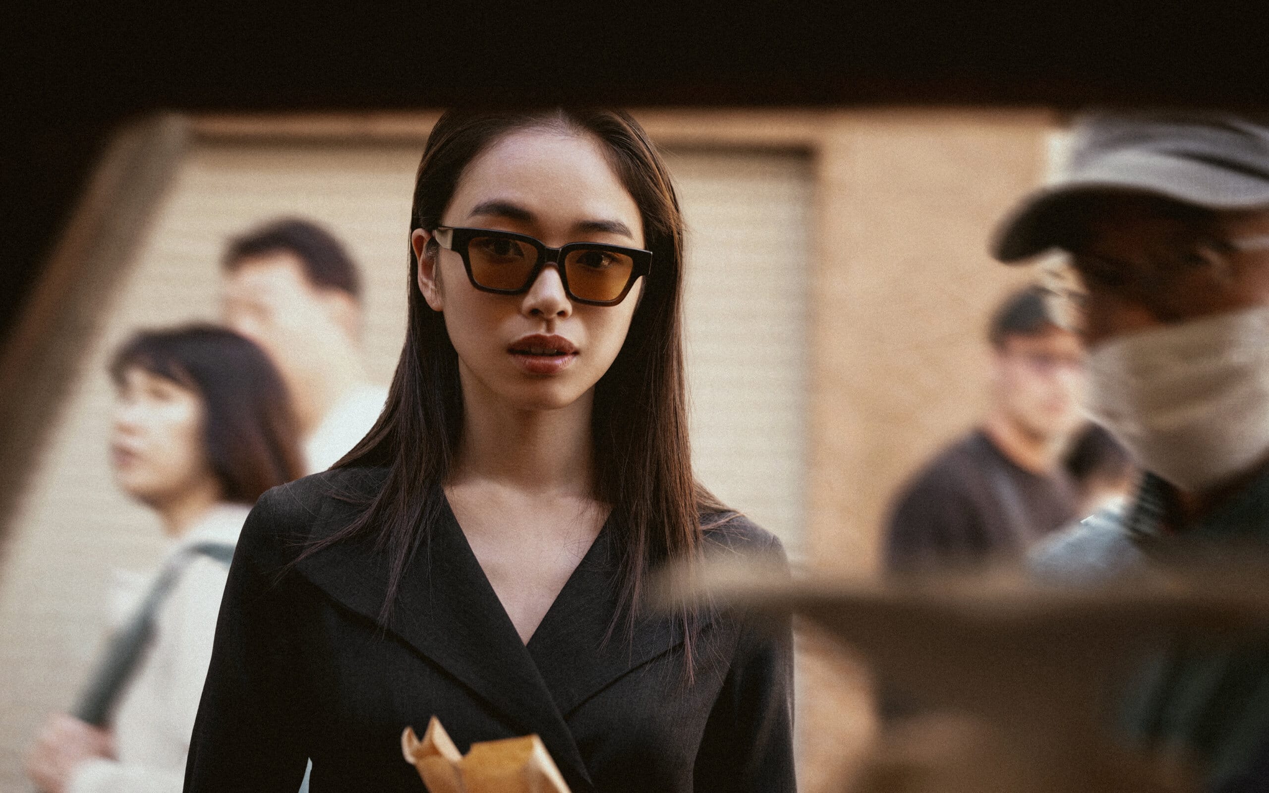 A woman wearing Nirvan Javan's Toronto shades stands amidst a Japanese street market, her gaze focused and confident, embodying the bold and dynamic design of the TORONTO Collection.